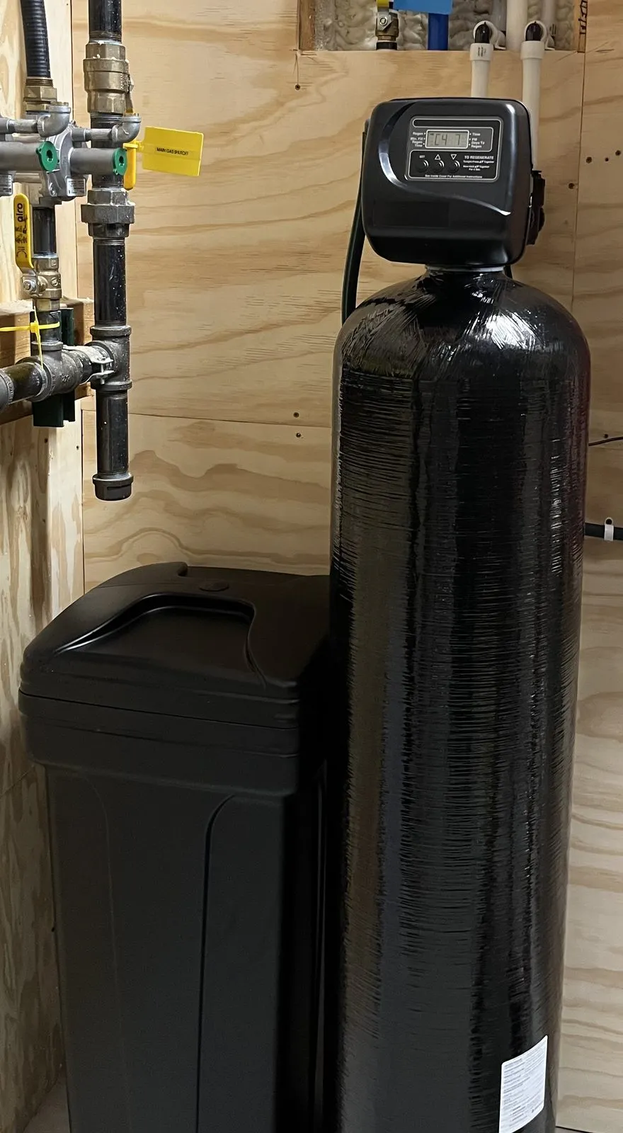 Mixed-bed media tank and brine tank installed against a plywood utility wall