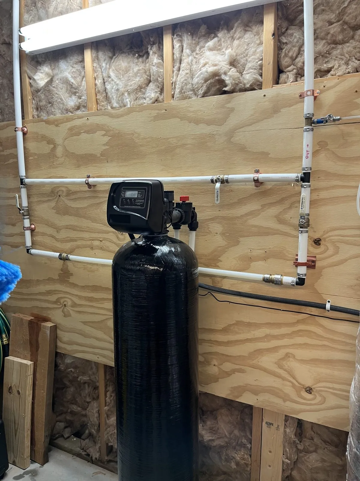 Carbon filter tank plumbed into the main line on a plywood wall